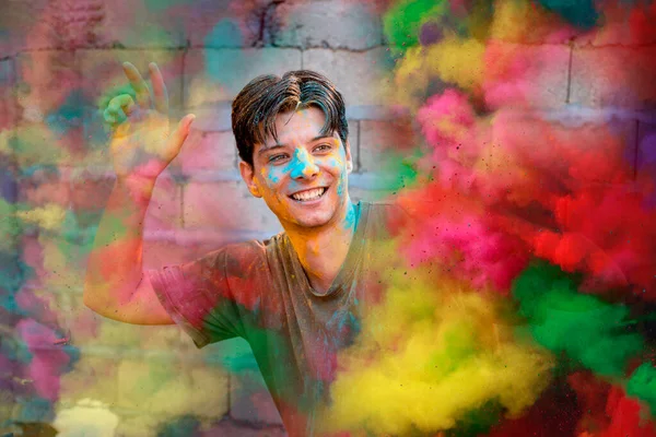 Young Man covered with Holi colors for Indian traditional festival on the street. Colorful handsome Man happy face outdoors looking at camera