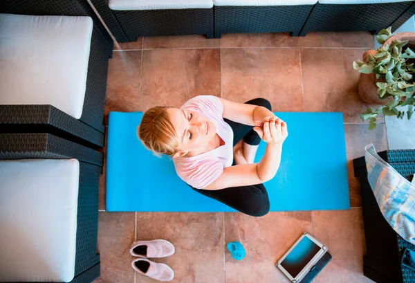 Woman meditate watching video tutorial online on tablet. Mid adult Female doing Yoga workout at home sitting on mat in living room