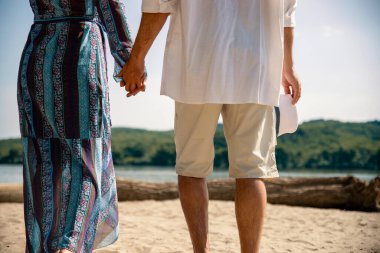 Olgun bir çift açık havada güneşli bir günde yürüyor. Kadın ve erkek el ele tutuşup nehir kıyısındaki kumsalda yürüyorlar. Boşluğu kopyala