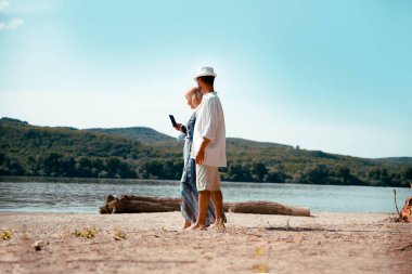 Olgun bir çift açık havada güneşli bir günde yürüyor. Kadın ve erkek el ele tutuşup nehir kıyısındaki kumsalda yürüyorlar. Boşluğu kopyala