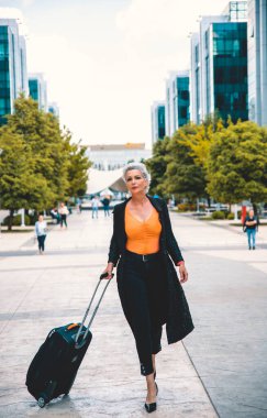 Topuklu giyen yaşlı beyaz saçlı kadın havaalanına bavuluyla gidiyor. Siyahlı kadın gezgin iş gezisine gidiyor, boşluğu kopyala