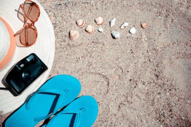 Güneş şapkası, fotoğraf makinesi, güneş gözlüğü, parmak arası terlik, havlu ve deniz kabuğu. Metin için alanı olan resmi kes. Yaz Tatili arkaplan pankartı şablonu