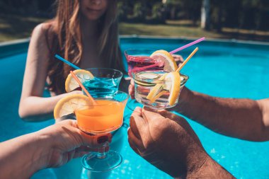 Hands of group of diverse People cheering toast holding colorful cocktails in the swimming pool. Close up