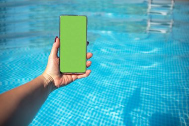Mavi havuz suyuna karşı dişi elinde krom anahtar yeşil ekranlı akıllı telefon. Reklam arkaplanı