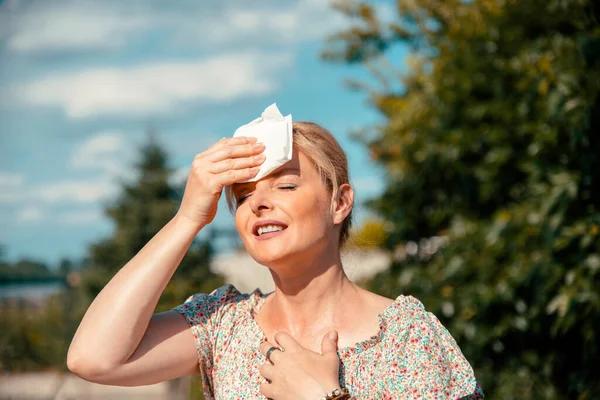 Woman feeling bad pain, heat, woman with heatstroke. Having sunstroke at summer hot weather. Mature Female under sunshine suffering from Headache. Person holds paper tissue on head