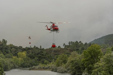 İtfaiye helikopteri orman yangınını söndürmek için bir kova su taşıyor.