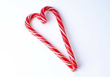 Beyaz çizgili iki kırmızı çubuk, açık arkaplanda kalp şekli oluşturur..