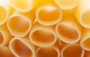 Makarna tüp şeklinde, yakın planda duruyor. Sarı arkaplan.