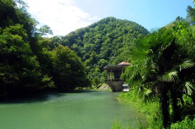 Abhazya dağlarında yeşil ağaçlar ve palmiyelerle çevrili bir göl. Eski tren istasyonu.