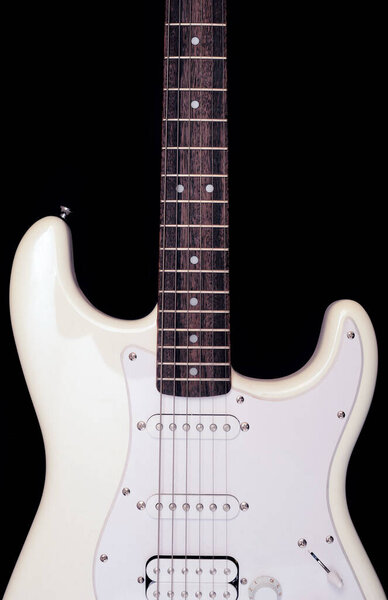 A fragment of the body of an electric guitar of white color on a black background close-up.
