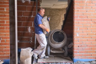 İnşaat işçisi beton karıştırıcıya kum torbası yüklüyor..