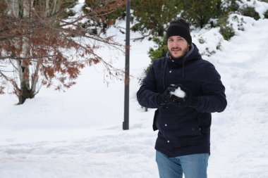 Genç beyaz bir adam parkta kartopu yapıyor.