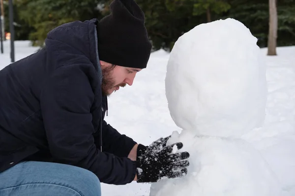Young caucasian man making a snowman — Stock Photo, Image