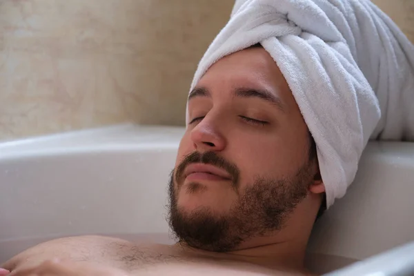 Молодий розслаблений чоловік з закритими очима лежить у білій ванні, наповненій гарячою водою . — стокове фото