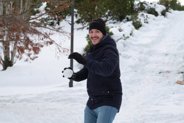Genç beyaz bir adam parkta kartopu atmaya hazır.