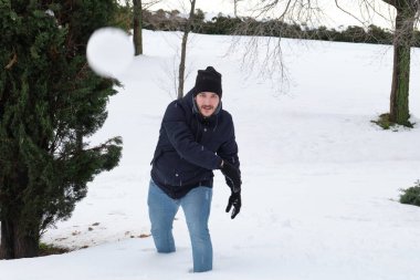 Genç beyaz bir adam parkta kartopu atıyor.