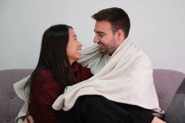 Genç mutlu çift battaniyeyle örtülmüş, kanepede oturuyorlar..