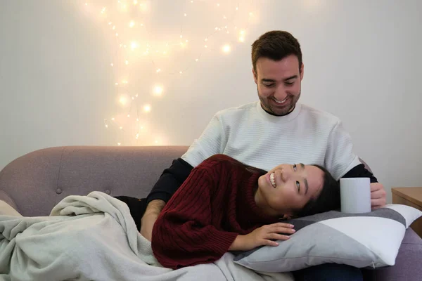 Joven feliz pareja multirracial mirándose y sonriendo en el sofá. — Foto de Stock