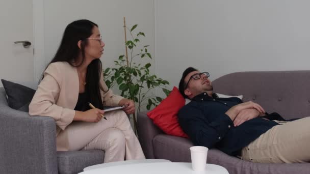 Aziatische vrouwelijke psycholoog luisteren naar haar Kaukasische man patiënt. — Stockvideo