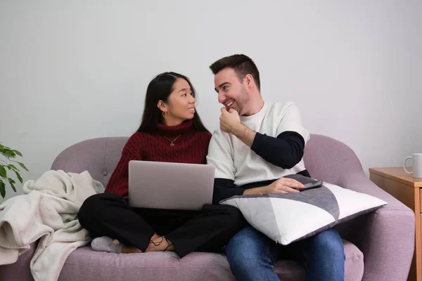 Joven pareja feliz relajarse en un sofá en casa usando el ordenador portátil y hablando. — Foto de Stock