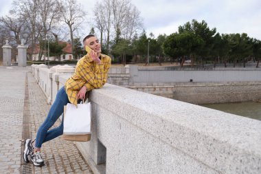 Makyajlı genç adam akıllı telefondan alışveriş torbalarıyla konuşuyor..