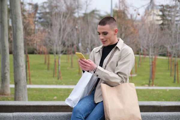 Молодий чоловік в макіяжі тримає сумки і спілкується на смартфоні . — стокове фото