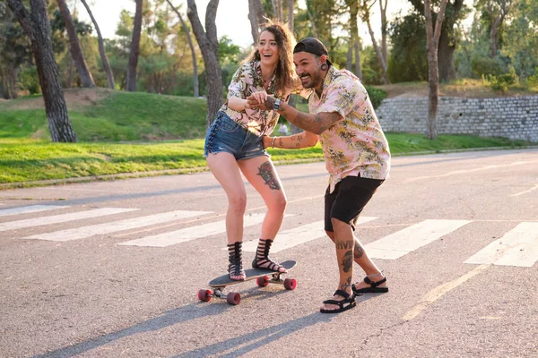 Junger cooler tätowierter Mann bringt seiner Freundin das Skateboarden bei. — Stockfoto