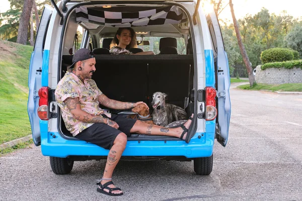 Genç ve dövmeli bir çift köpekleriyle minibüsün arkasında oturuyor..