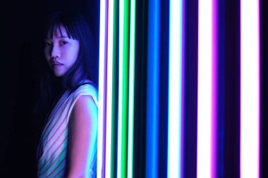 Genç Asyalı kadın stüdyoda renkli parlak neon ışıklarla poz veriyor..