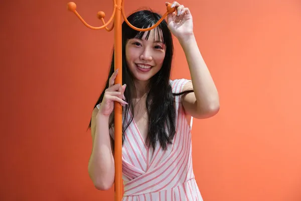 Junge asiatische Frau posiert mit einem rot-orangen monochromen Kleiderständer. Studioaufnahme. — Stockfoto