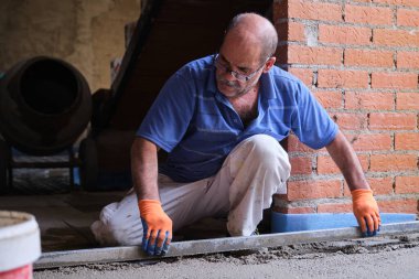 İnşaat işçisi, parlayan zeminin üstündeki betonu düzleştiriyor..