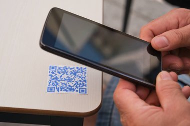 Akıllı telefonu kullanarak bir bar masasındaki QR kodunu tarayan bir adam..