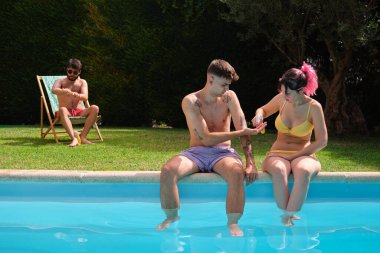 Üç beyaz arkadaş havuz kenarında güneş kremi sürüyor..
