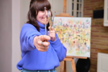 Yüzünün önünde fırça tutan mutlu genç bir kadın, seçici bir odaklanma..