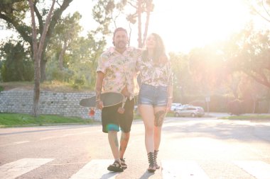 Genç, havalı dövmeli çift kaykayla birlikte yürüyor..