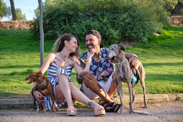 Молодая татуированная пара обнимается и сидит со своими собаками. — стоковое фото