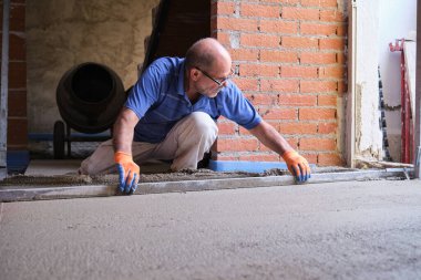 İnşaat işçisi zeminin altındaki betonu düzleştiriyor..