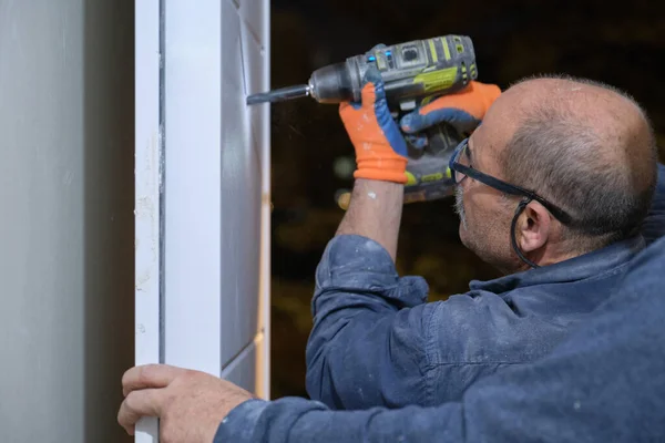 Trabajador senior instalando una mirilla en una puerta nueva usando un taladro. —  Fotos de Stock