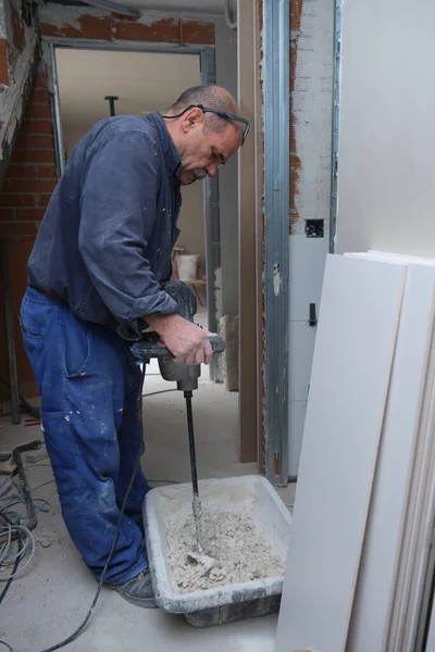 Kıdemli inşaat işçisi bir el mikseri ile fayans yapıştırıcı havan hazırlıyor..