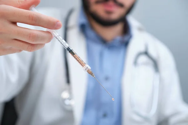 Médecin méconnaissable tenant une seringue avec un liquide orange. — Photo