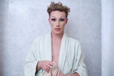 Bornoz giyen travesti banyoda kameraya bakıyor..