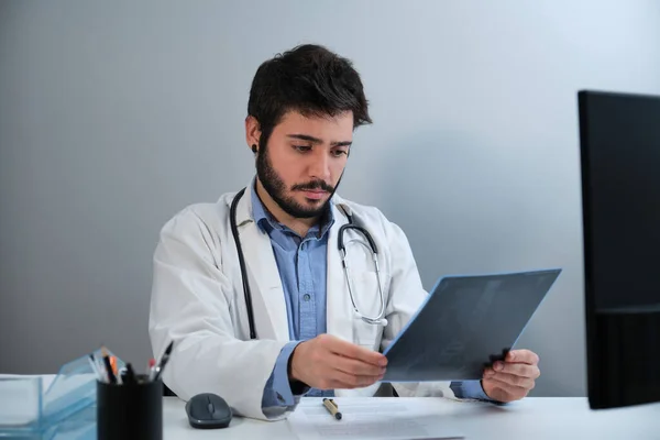 Médico joven mirando una radiografía de pelvis y columna vertebral en el escritorio. —  Fotos de Stock