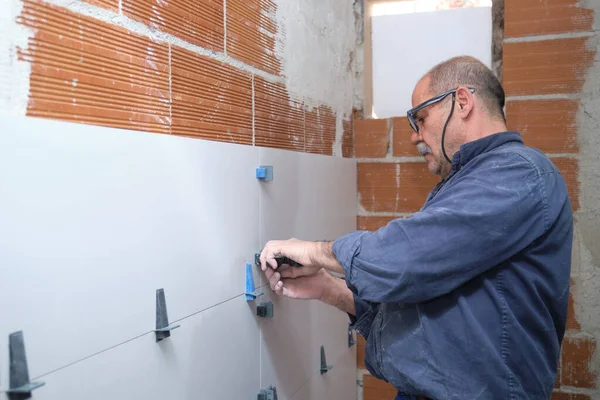 Obrero constructor senior ajustando la separación entre baldosas en la pared. —  Fotos de Stock