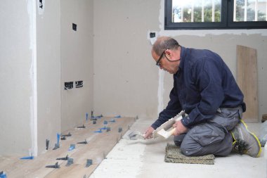 Senior tiler, mala ve çentikli malayla yere yapıştırıcı döşedi..