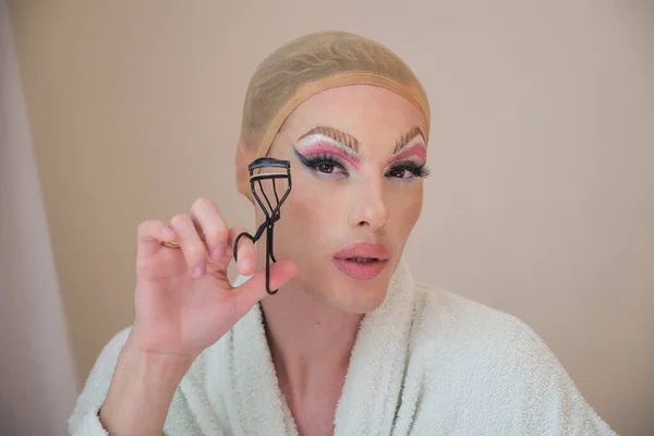 Drag queen person curling the lashes with a eyelash curler and wearing bathrobe. — Stock Photo, Image