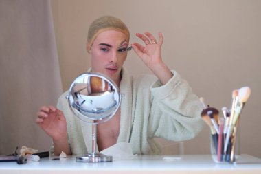 Travesti kadın takma kirpiklerini çıkarıyor ve bornoz giyiyor..