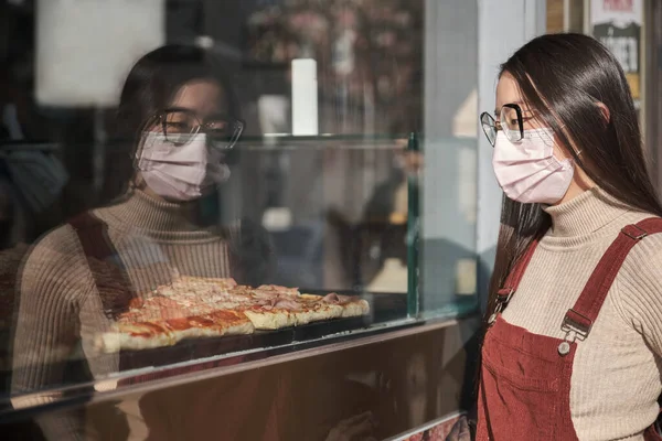 Joven mujer asiática usando mascarilla mirando una pizzería escaparate. — Foto de Stock