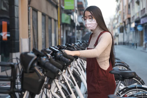 Joven mujer asiática usando mascarilla alquilando una bicicleta en la estación de alquiler. — Foto de Stock