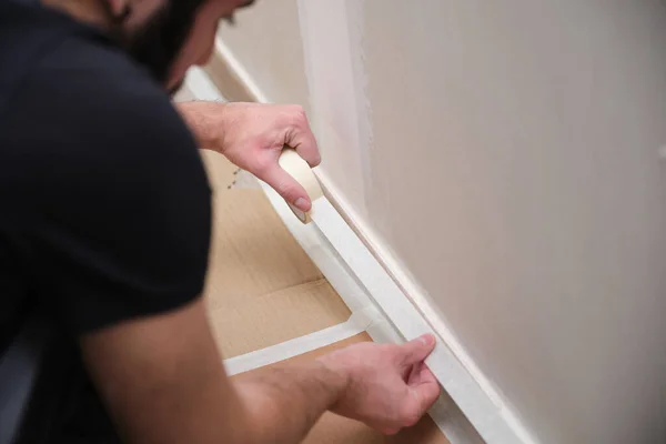 Pintor irreconocible usando cinta adhesiva para cubrir el zócalo antes de pintar. —  Fotos de Stock