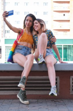 Gülümseyen ve dışarıda selfie çeken genç lezbiyen çift..